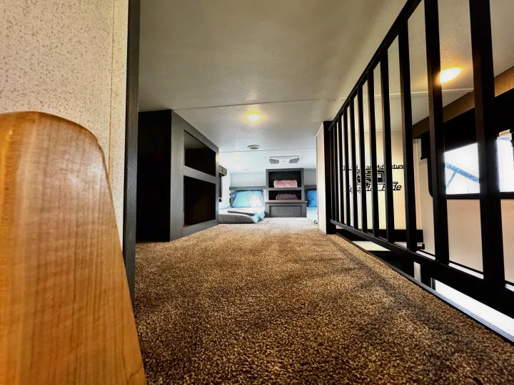 Inside an RV rental, a cozy, carpeted loft area views bunk beds and a functional sleeping space with modern dark wood accents.. Forest River Puma Destination 2026