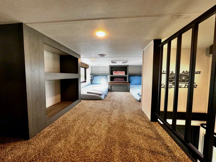 Spacious RV rental bunkhouse: modern bunk beds, two additional beds, cozy carpeted floor, and safety railing.. Forest River Puma Destination 2026