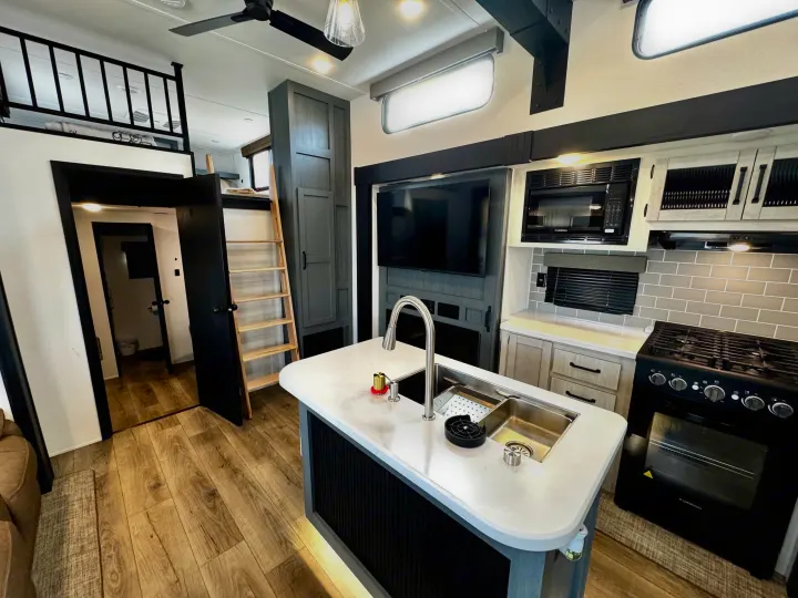 Spacious RV rental interior featuring a modern kitchen with island sink, stove, microwave, and upper loft area.. Forest River Puma Destination 2026