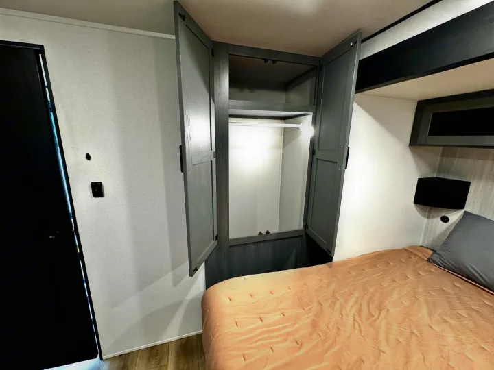 Cozy RV rental bedroom: open wardrobe, bed with peach comforter & gray pillow, small nightstand.. Forest River Puma Destination 2026