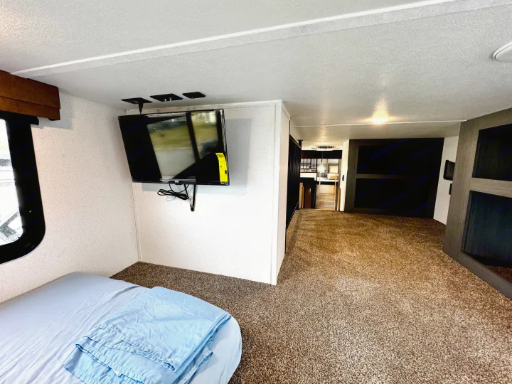 Comfortable RV rental bedroom with a mounted TV, soft bed, and plush carpet, looking towards the bunk area.. Forest River Puma Destination 2026