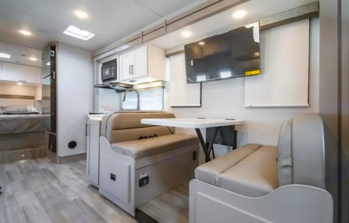Bright RV rental interior features a kitchen, dinette, TV, and comfortable bedroom, ideal for your next adventure.. thor four winds 2027