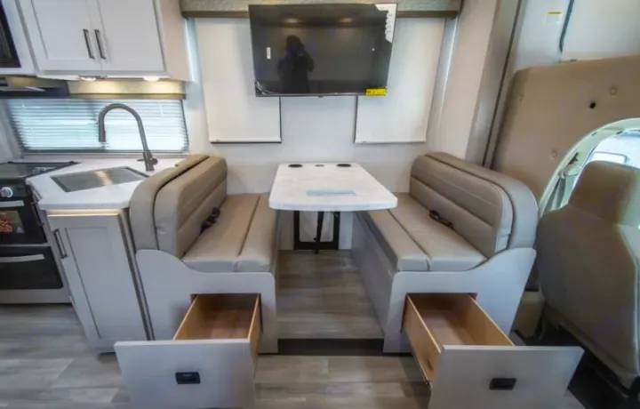 RV rental interior featuring a bright dinette with open storage drawers, a kitchen area, and a wall-mounted TV.. thor four winds 2027