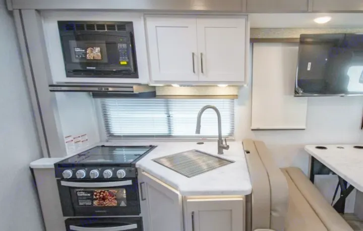 RV rental interior featuring a compact kitchen with microwave, stove, sink, and an adjacent dinette with TV.. thor four winds 2027