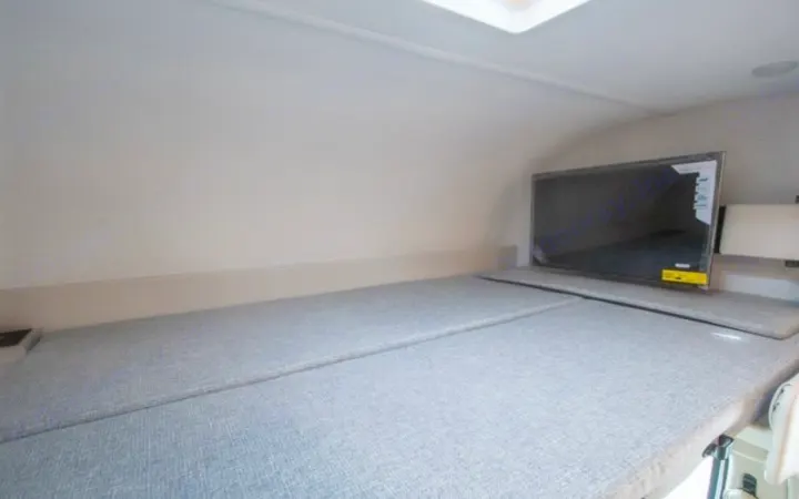 Experience comfort in this RV rental! Features a plush sleeping area with a gray upholstered bed and a flat-screen TV for relaxing.. thor four winds 2027