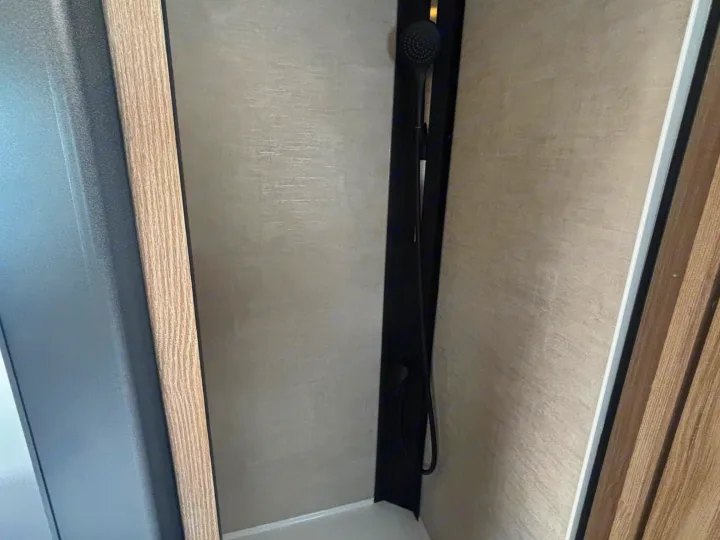 Modern RV rental shower interior, featuring a black shower head, light textured walls, and wood-look trim.. FORD TRANSIT RIMOR KILIG 669 5 BERTH 2026