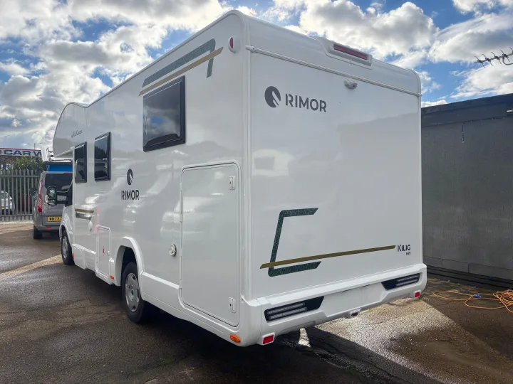 A sleek white Rimor Kilig 669 campervan, ideal for an RV rental adventure, is parked outdoors, showcasing its side and rear under a cloudy sky.. FORD TRANSIT RIMOR KILIG 669 5 BERTH 2026