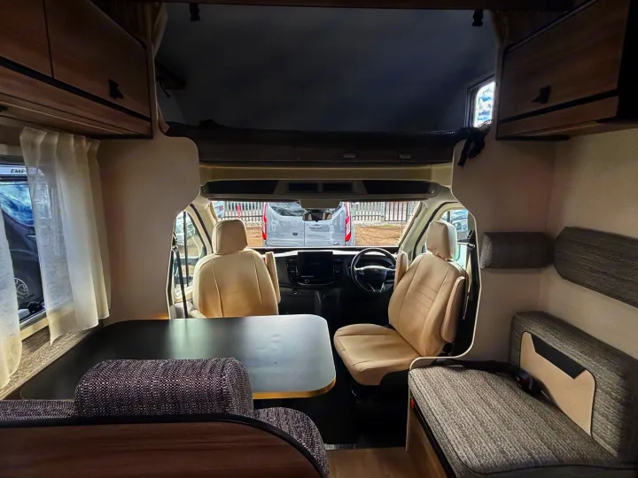 Inside a spacious RV rental: view from the rear, showing dining area, swiveling front seats, and overhead bed.. FORD TRANSIT RIMOR KILIG 669 5 BERTH 2026