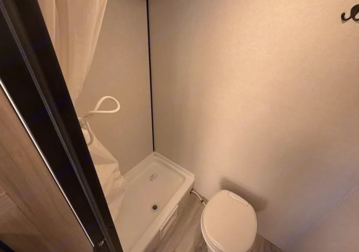 RV rental bathroom: compact space with a bright white shower stall, curtain, and toilet.. Keystone Coleman 2026