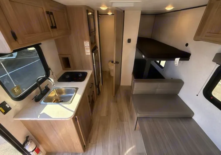 Inside a modern RV rental: Kitchenette, dining space, bunk bed, and a peek into the bathroom. Ready for your next adventure.. Keystone Coleman 2026