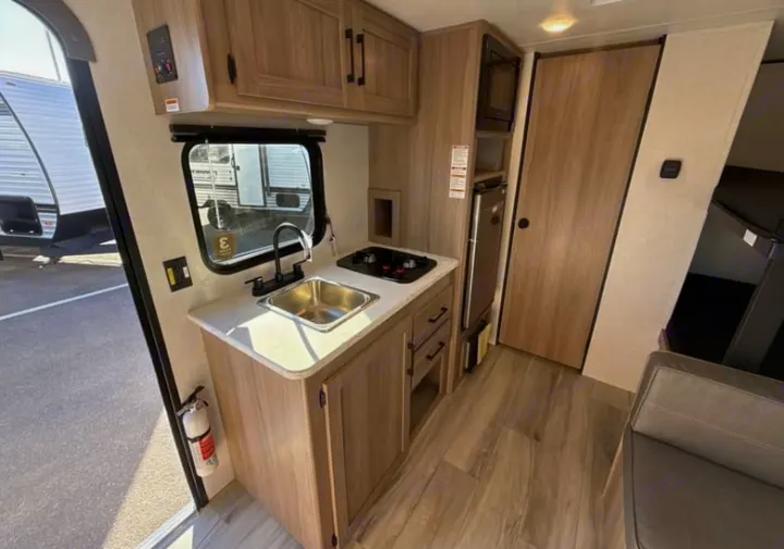 This RV rental interior showcases a functional kitchen with sink, stove, microwave, fridge, and cozy living/sleeping areas.. Keystone Coleman 2026