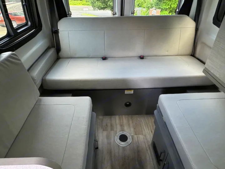 Comfortable RV rental interior with light gray bench seats and a floor table mount. A spacious camper van dinette area.. Thor Dazzle 2025