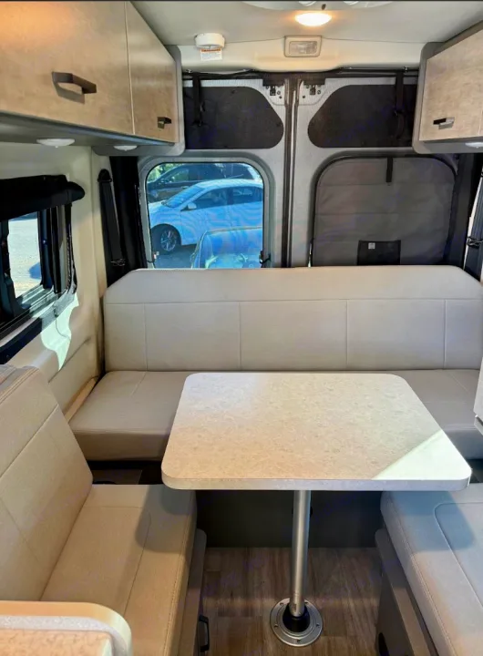 Spacious RV rental interior with a dinette, bench seating, overhead storage, and large windows. Perfect for your next road trip.. Thor Dazzle 2025