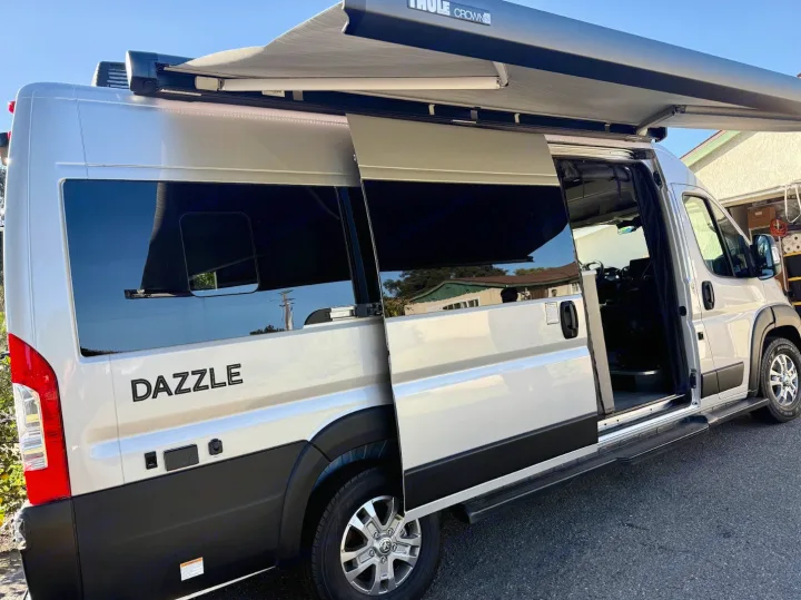 Bright silver 'DAZZLE' camper van with an extended Thule awning and open side door, perfect rv rental for adventures.. Thor Dazzle 2025