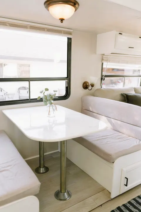 Cozy RV rental dining nook featuring a white table, cushioned benches, and bright windows. Ideal for comfortable meals inside.. Coachmen Catalina 2012