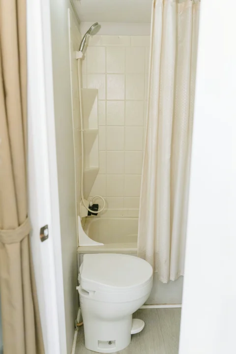 Inside an RV rental, a compact bathroom features a white toilet, small shower/tub, and light-colored shower curtain.. Coachmen Catalina 2012