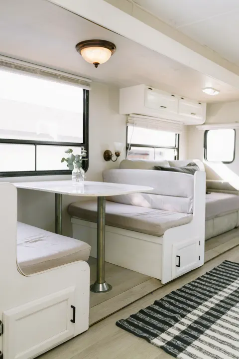 Bright RV rental interior: a modern dinette with light cushions, small plant, and striped rug on wood-look flooring.. Coachmen Catalina 2012