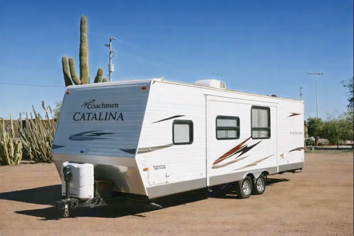 White Coachmen Catalina travel trailer for **rv rental**, parked in a sunny desert landscape with saguaro cacti visible.. Coachmen Catalina 2012