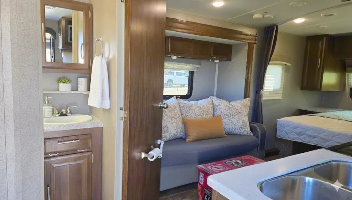 Explore this RV rental's inviting interior with a functional bathroom vanity, cozy living area, kitchen sink, and comfortable bed.. Forest River Rockwood Mini Lite 2020
