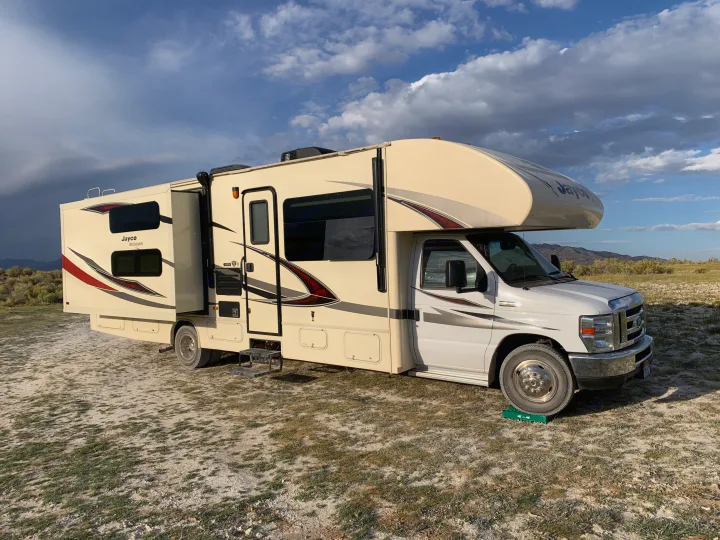 A cream-colored Jayco Redhawk Class C rv rental with its slide-out open, parked on a dirt road in a scenic, natural landscape.. Jayco Redhawk 31X 2017