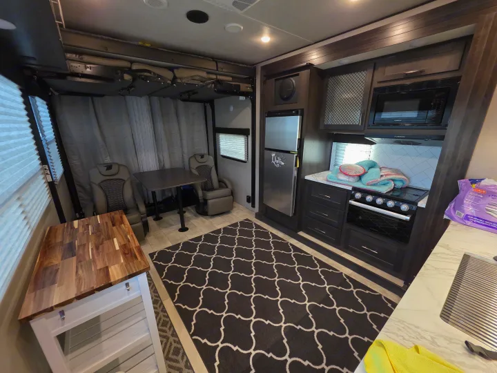 RV rental interior: a modern kitchen, dining with recliners, and tucked-away overhead bunks provide comfort.. Grand Design Momentum Toy Hauler 2022