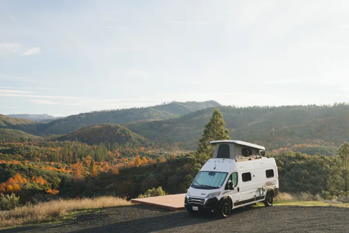 White RV rental camper van with a pop-top, parked at a scenic overlook, surrounded by vibrant autumn mountains.. Winnebago Winnebago 2026