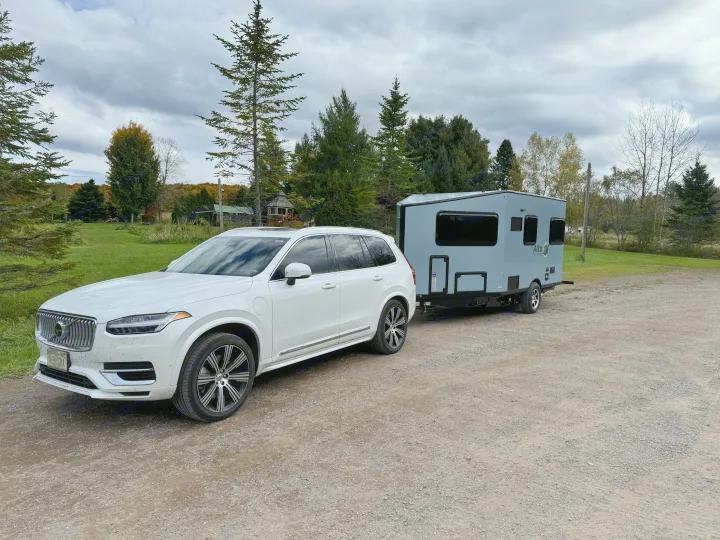 White Volvo SUV towing a sleek gray RV rental, parked on a gravel road, ready for a nature getaway under cloudy skies.. Safari Condo A2124 2025