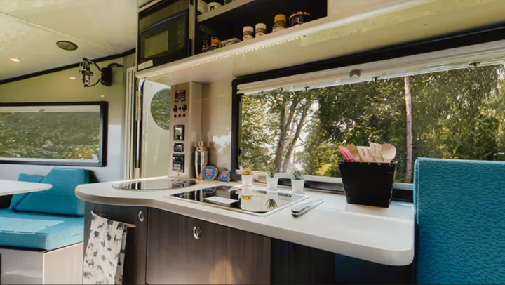 Modern RV rental kitchen featuring a sink, stove, microwave, and cozy blue seating. Enjoy mobile living with nature views.. Safari Condo A2124 2025