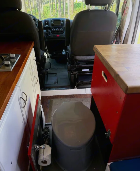 RV rental interior: cockpit, left kitchenette with stovetop, and portable toilet. Compact camper van setup.. Ram Promaster 2500 2019