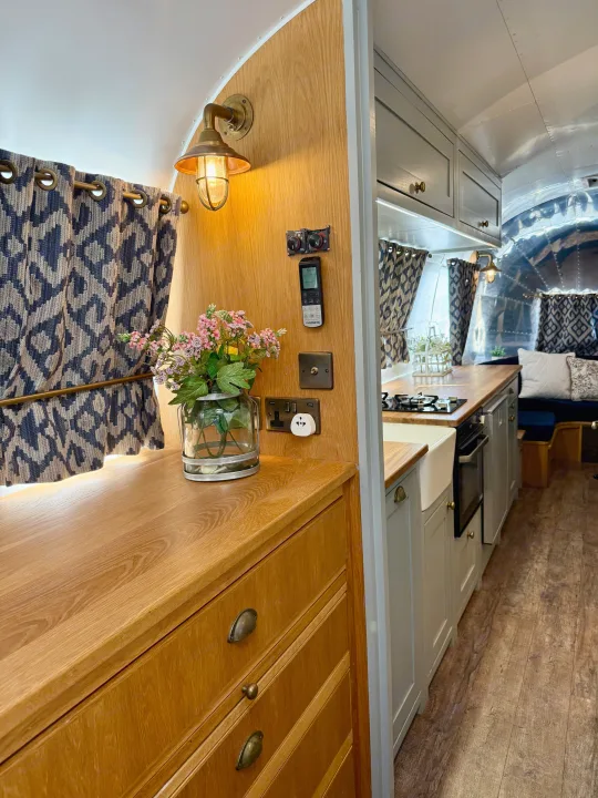 Cozy Airstream RV rental interior featuring warm wood finishes, patterned curtains, and a well-appointed kitchen area with a farmhouse sink.. Airstream overlander 2018