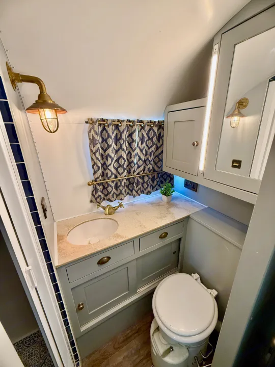 Stylish RV rental bathroom featuring a sink, vanity, toilet, brass fixtures, mirror, and patterned curtain.. Airstream overlander 2018