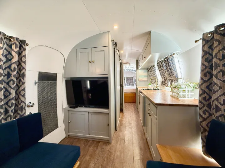 Cozy Airstream RV rental interior: living space with TV, full kitchen, and bedroom view. Modern travel trailer design.. Airstream overlander 2018