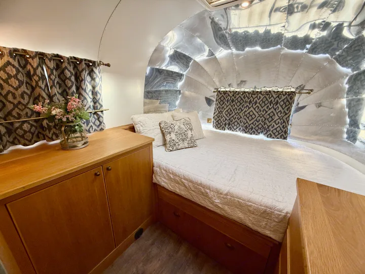 Cozy RV rental bedroom with a comfy bed, wooden cabinetry, patterned curtains, and signature metallic Airstream walls.. Airstream overlander 2018