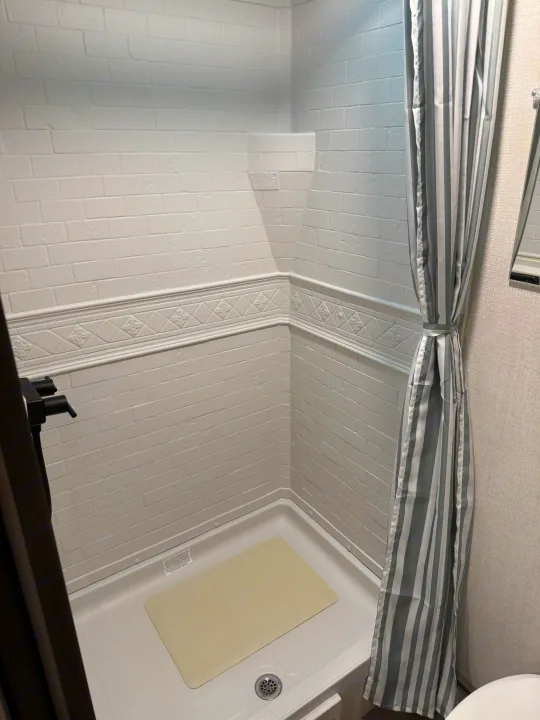 Inside this RV rental, find a clean, compact shower: white brick walls, decorative trim, white pan, and striped curtain.. Grand Design Transcend One 2025