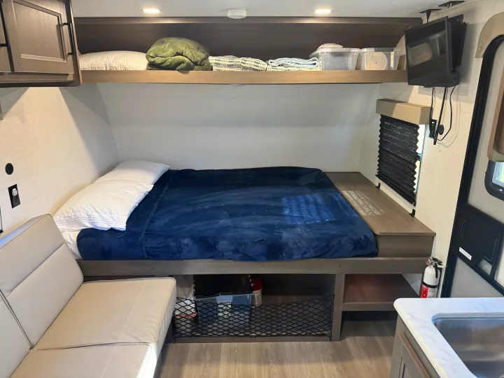 Cozy RV rental interior: bed with storage, sofa, and overhead cabinets for a comfortable stay.. Grand Design Transcend One 2025
