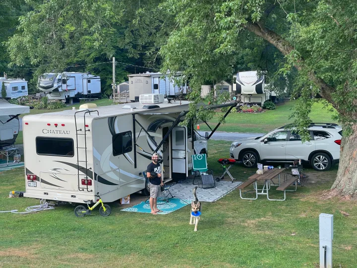 A family enjoys their **rv rental** at a scenic campground. Man, child, and dog revel in outdoor leisure, surrounded by trees.. Thor Motor Coach Chateau 2017