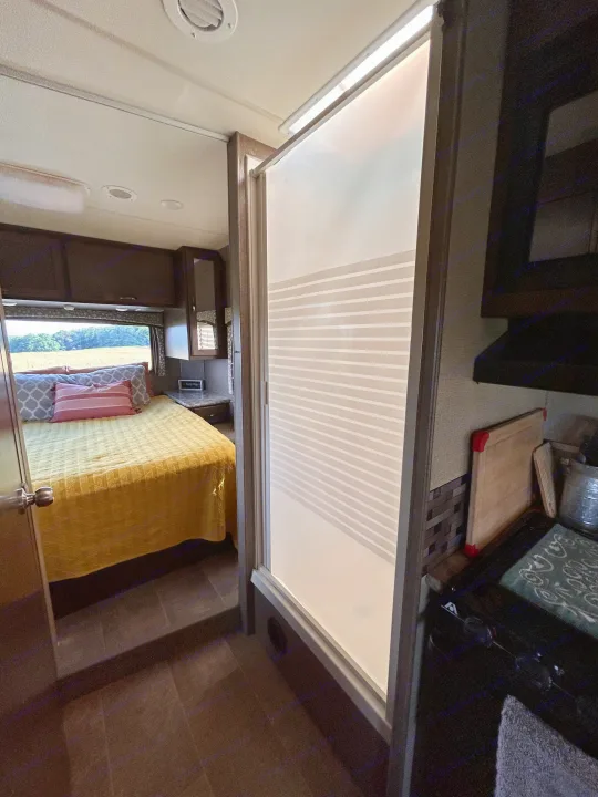 Cozy rv rental interior showing a bedroom with a yellow quilt, kitchen area, and a frosted privacy screen.. Thor Motor Coach Chateau 2017