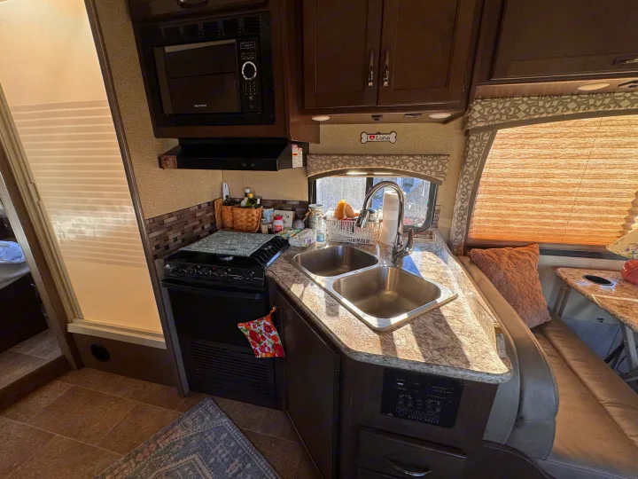 This bright RV rental kitchen features a microwave, stove, double sink, and inviting dinette area with natural window light.. Thor Motor Coach Chateau 2017