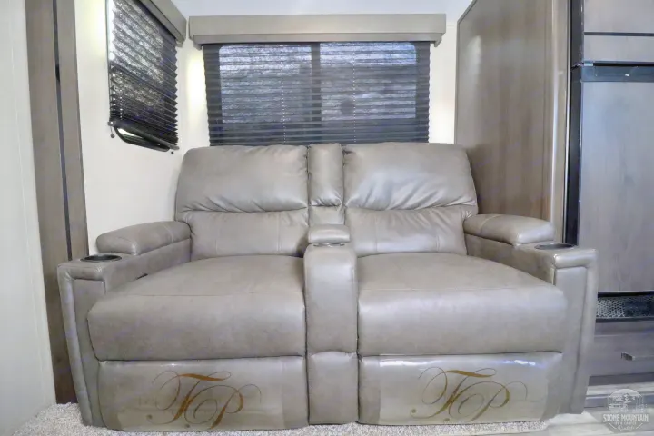 Relax in this RV rental's gray reclining loveseat with cup holders, next to windows with dark blinds.. Grand Design Transcend Xplor 2023