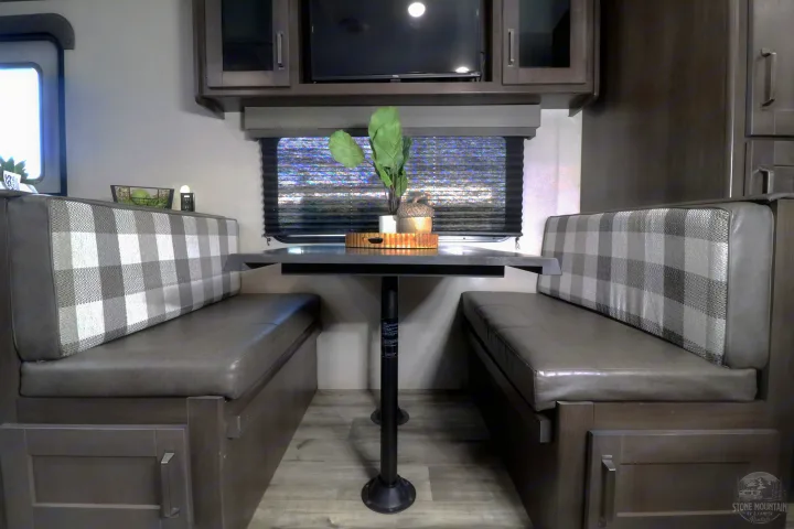 Step inside this RV rental's dinette area featuring comfortable plaid bench seating, a dark table, and ample storage.. Grand Design Transcend Xplor 2023