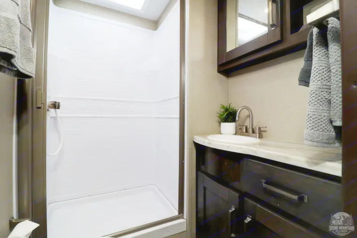 Clean RV rental bathroom features a spacious shower with decorative trim and a modern vanity with sink, perfect for your travels.. Grand Design Transcend Xplor 2023