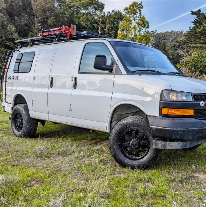 White 4x4 adventure van, with off-road tires, roof rack, and rear ladder, available for rv rental exploration.. Chevrolet Express 2019