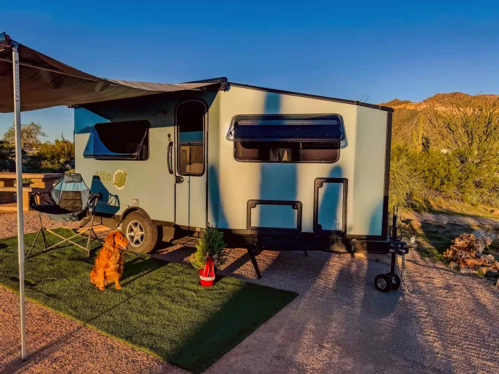 Pet-friendly rv rental adventure! A light blue travel trailer, dog, and small Christmas tree on artificial grass in a sunny desert campsite.. Safari Condo A2124 2025