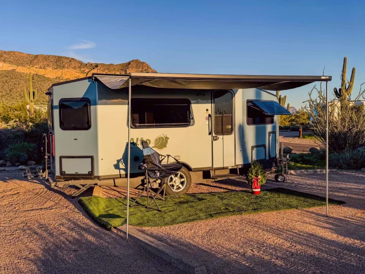 Light blue RV rental camper with extended awning, chair, and holiday decor at a desert campsite with mountains and cacti.. Safari Condo A2124 2025