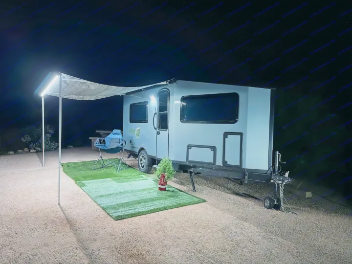 Cozy rv rental travel trailer campsite at night with an illuminated awning, artificial grass, camping chair, and festive mini tree.. Safari Condo A2124 2025