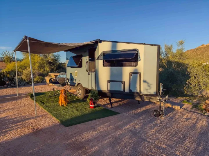 Our RV rental provides cozy camping! A golden retriever and a small festive tree under the awning in a sunny desert spot.. Safari Condo A2124 2025