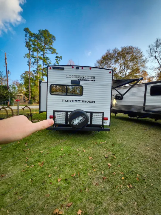 Back of a white Cherokee Grey Wolf travel trailer, great for an RV rental. A hand points to its spare tire & rack.. Forest River Cherokee Grey Wolf 2025