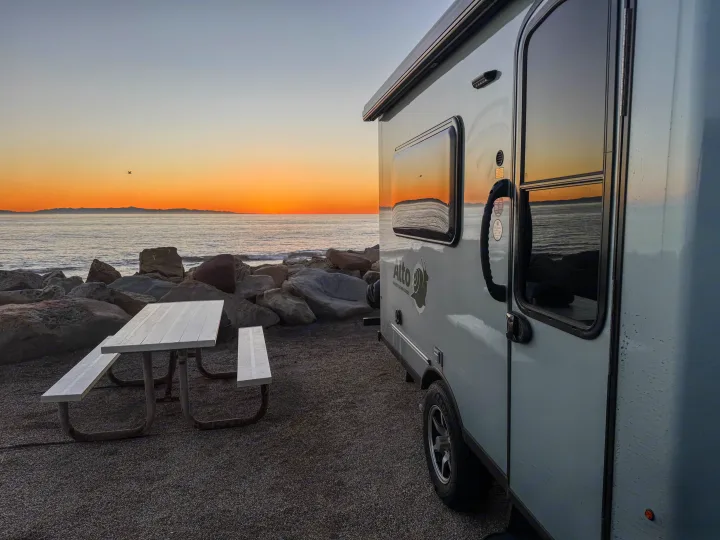 RV rental by the ocean at sunset. A modern camper and picnic table offer stunning beach views, perfect for memorable camping trips.. Safari Condo A2124 2025