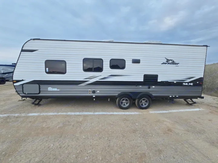A modern white and gray Jay Flight SLX RV rental, parked on a dirt lot under a cloudy sky, ready for your camping or road trip.. Jayco Jay Flight SLX 2022