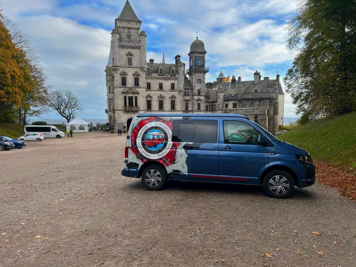 Blue Tartan Camper Co. **rv rental** by majestic Dunrobin Castle, Scotland, under cloudy skies. A blue campervan on gravel, ideal for historic Scottish travel.. Volkswagen T5 2018